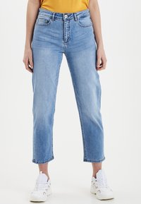 Light blue denim jeans, straight cut, high-rise waist, front pockets, and stitched details. Paired with white sneakers for contrast.