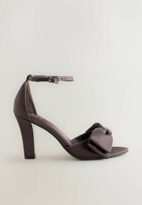 Brown satin hoge hak schoen met enkelbandje, met een strikaccent op de teen en een gladde textuur. Gesloten achterkant ontwerp.