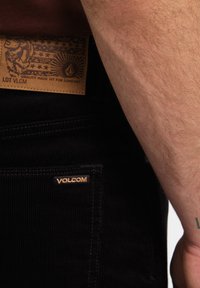 Sorte kordfløjspants med et læder Volcom mærke med en præget design, placeret ved bindebåndet, samt et lille Volcom-logo på lommen.