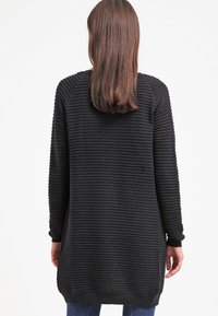 Schwarzer Pullover mit geripptem Material, langen Ärmeln und Kapuze. Hat eine lockere Passform und reicht bis zur Mitte des Oberschenkels. Einfaches Design ohne zusätzliche Muster.