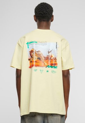 Yellow cotton t-shirt featuring a graphic print of a leopard and antelope on the back, with green and red accents and various logo details.