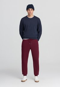 Felpa navy con scollo a tondo, pantaloni jogger bordeaux con vita regolabile, e sneakers bianche; texture liscia, design casual.