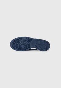Marinblå sneakersula med texturerat gummi, utrustad med cirkulära och linjära mönster för grepp, präglad logotyp på sidan.