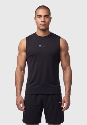 Uomo atletico che indossa una canotta nera Champion e pantaloncini coordinati, in piedi con espressione neutra su sfondo semplice.