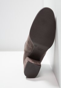 Botte à chevilles en suède gris avec une semelle en caoutchouc texturé et un talon épais. Présente un design incurvé et des accents de couture sur les côtés.