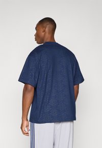 Camiseta azul marino con un patrón geométrico, de manga corta y corte relajado. Fabricada en material suave, presenta un cuello redondo clásico.