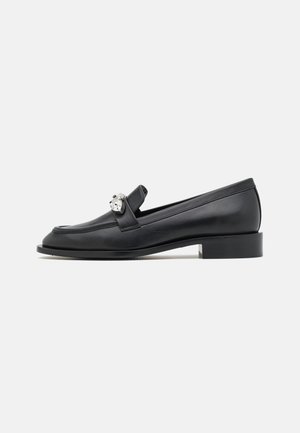 Mocassin en cuir noir avec un petit talon carré et un détail chaîne argentée sur le côté, montré de profil sur fond blanc.