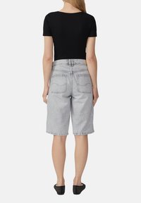 Zwarte geribbelde top met korte mouwen en ronde hals, gecombineerd met lichtgrijze denimshorts met een losse pasvorm en achterzakken.