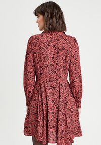 Robe florale rouge à manches longues, ornée d'un motif paisley noir, avec une taille cintrée, une jupe plissée et une texture de tissu douce.