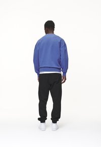 Felpa viola con vestibilità over e polsini a coste, abbinata a pantaloni della tuta neri e sneakers bianche. Tessuto testurizzato, design semplice.