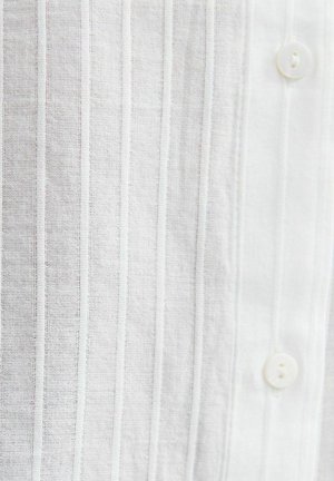Witte stof met verticale, gestructureerde strepen en twee witte knopen erop genaaid, met een gedetailleerde weergave van het fijne geweven materiaal.