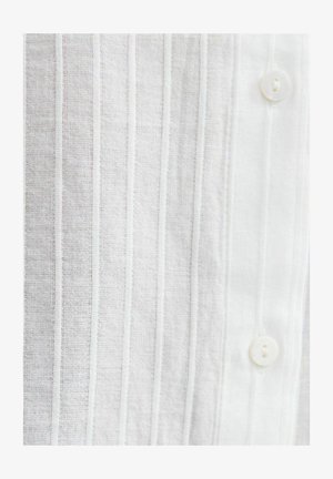 Witte stof met verticale, gestructureerde strepen en twee witte knopen erop genaaid, met een gedetailleerde weergave van het fijne geweven materiaal.