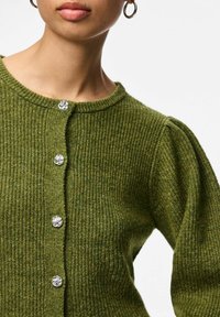 Zielony, dziergany kardigan z okrągłym dekoltem, teksturowanym prążkowaniem i srebrnymi kwiatowymi guzikami z przodu. Bufiaste rękawy nadają mu objętości.