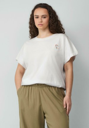 T-shirt en coton blanc avec un col rond et des manches courtes, présentant un design de broderie florale sur le côté gauche de la poitrine. Assorti à un pantalon vert olive.