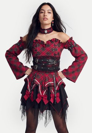 Young woman wearing a red plaid off-shoulder dress with black lace details, wide sleeves, and multiple belts around the waist.