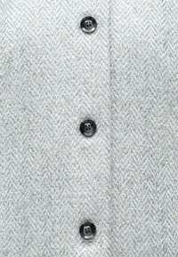 Lyseblåt fiskebensmønsterstof med en tekstureret overflade, der har fem sorte knapper langs midten til lukning.