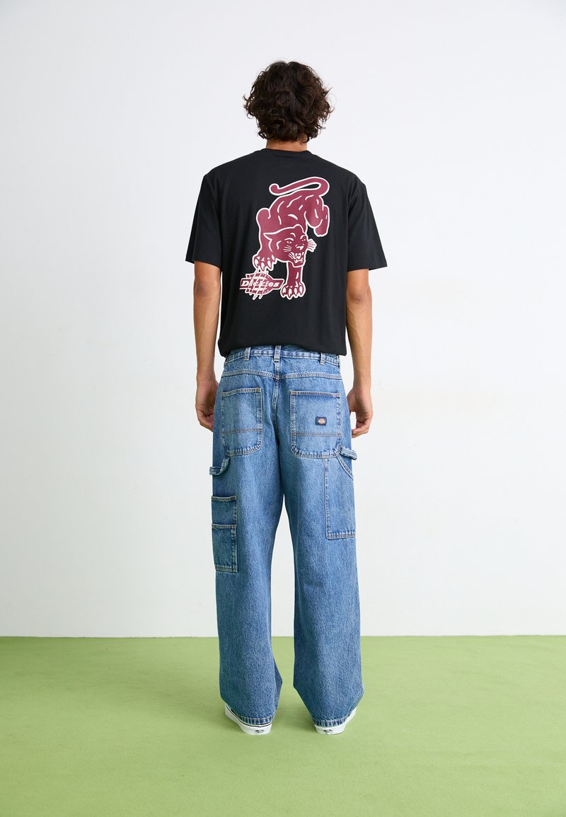 Schwarzes Grafik-T-Shirt mit einem roten Pantherdesign auf dem Rücken, kombiniert mit hellblauen, weiten Cargo-Jeans mit mehreren Taschen.