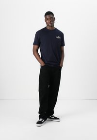 Navy cotton t-shirt with a round neckline and small logo, paired with loose black pants and black sneakers with white accents.