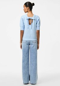 Ljusblå stickad tröja med en rosett bak, korta ärmar och vid halsringning, i kombination med högmidjade vida denimjeans.