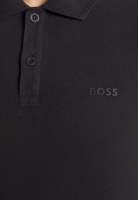 Polo noir à col avec deux boutons et logo "BOSS" brodé sur la partie supérieure gauche de la poitrine.