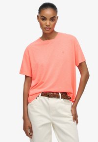 Kortærmet T-shirt med rund hals i neongrøn. Blød tekstur med en lidt løs pasform, parret med lysfarvede bukser og et fletbrunt bælte.