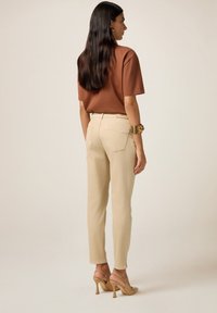 Camisa marrón de manga corta combinada con pantalones de cintura alta beige y sandalias de tacón beige, con bolsillos traseros y una textura suave.