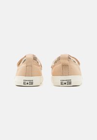 Zapatillas de lona beige con un diseño de corte bajo, suelas de goma blanca y un logo negro de "Converse All Star" en la parte trasera.