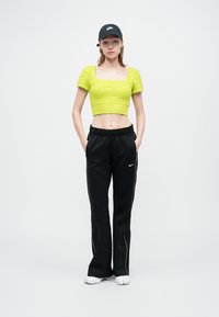 Neon zelený krátky pletený top s hranatým výstrihom, v kombinácii s čiernymi teplákmi s bielymi bočnými pruhmi a čiapkou Nike.