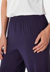 Marineblauwe broek met elastische tailleband, gemaakt van zachte stof, met een gladde textuur en een aansluitend ontwerp, getoond met een hand erop rustend.