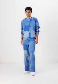 Blå tröja och byxor i mjukt tyg, med stora ljusblå blommönster. Tröjan har en kontrasterande vit krage och manschetter.