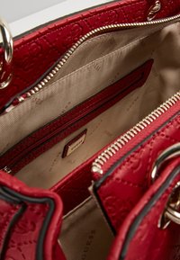 Rode gequiltte handtas met een gladde textuur, voorzien van een crèmekleurig interieur en een ritsvak met een merklabel. Inclusief accenten in zilver.
