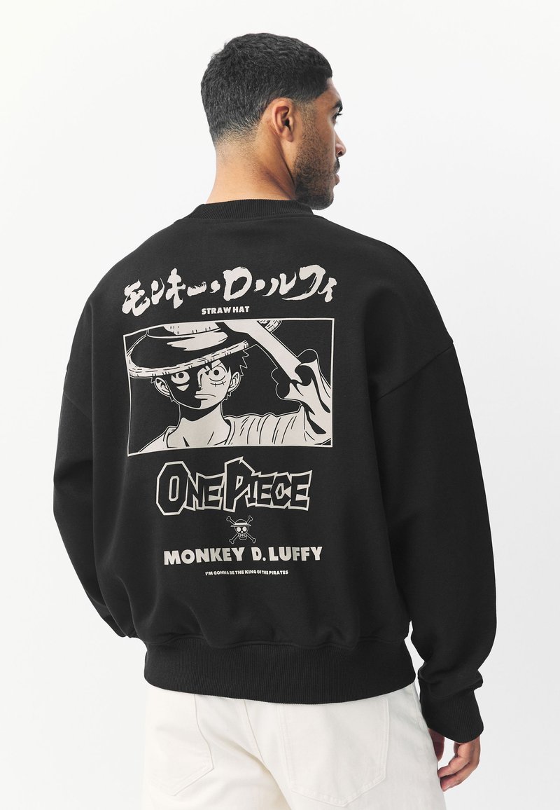 Sort sweatshirt med et grafisk tryk af en karakter med en stråhat på ryggen. Teksten inkluderer "ONE PIECE" og "MONKEY D. LUFFY."