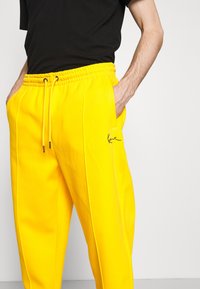 Gelbe Trainingshosen mit elastischem Bund und Kordelzug, ausgestattet mit seitlichen Taschen und schwarzem Logo-Logostick. Glatte Textur, lockere Passform.