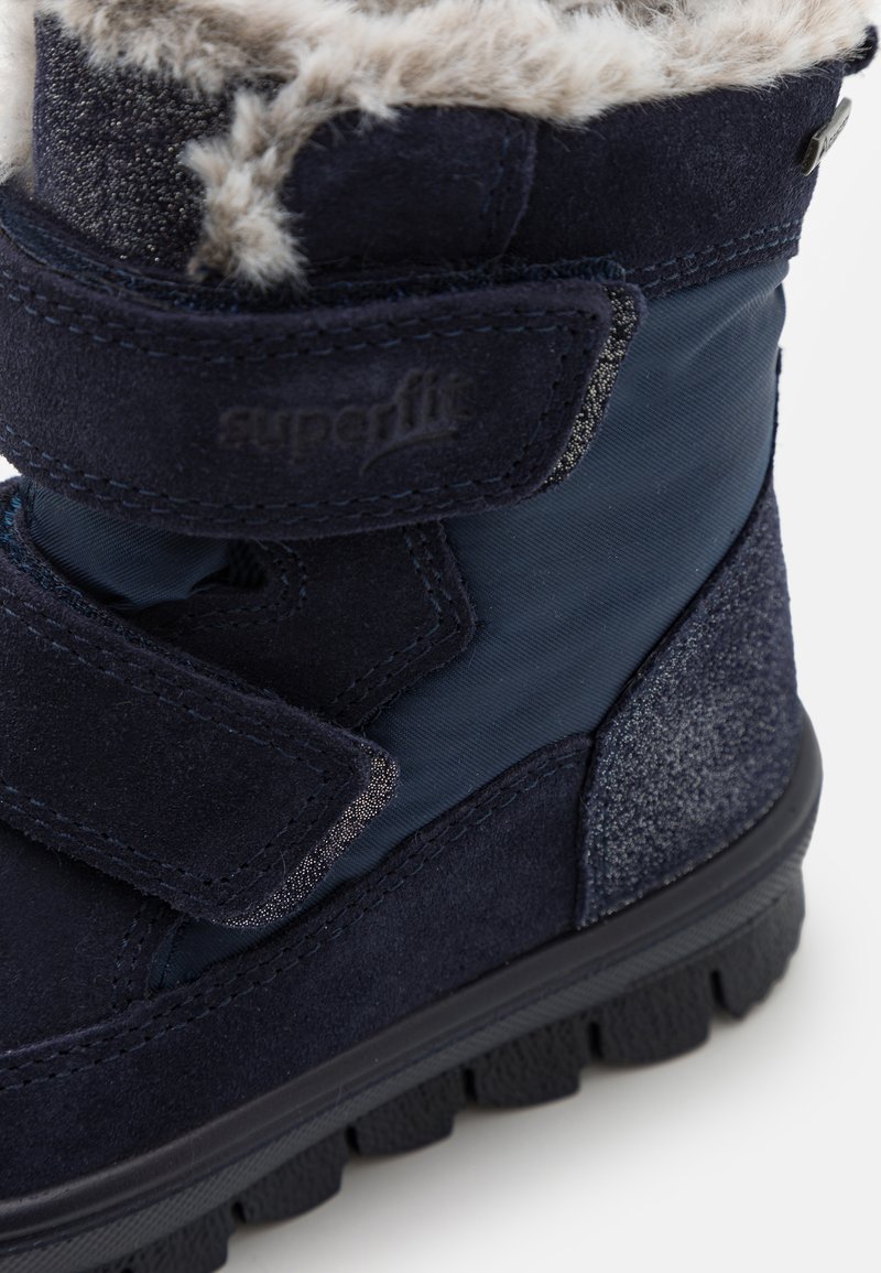 Marineblaue Winterstiefel mit Klettverschluss, Obermaterial aus Wildleder und Textil, mit Fellfutter, strukturierten Sohlen und subtilen Glitzerelementen.