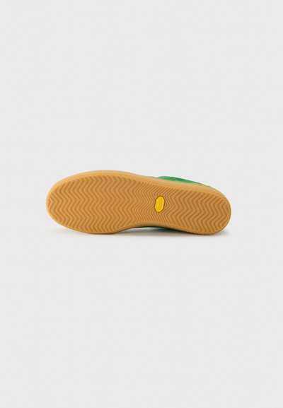 Semelle de chaussure verte avec un motif en zigzag, en caoutchouc. Présente un accent jaune et une finition texturée pour une meilleure adhérence.
