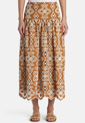 Hnedá midi sukňa s bielym kvetinovým čipkovým výšivkom, s oblým lemom, nosená s tkanými sandálmi s otvorenou špičkou a bielym topom.