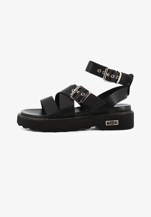 Sandali neri caratterizzati da molteplici design di strap e una suola chunky. Accentuati da fibbie argentate e un pattern di battistrada evidente sulla suola.