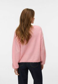 Ροζ φαρδύ πουλόβερ με απαλή υφή, άνετη εφαρμογή και μακριά μανίκια. Φορεμένο με σκούρο τζιν, φωτογραφημένο από πίσω.