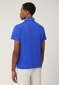 Polo blu con maniche corte, texture uniforme e colletto con un accento bianco. Il retro ha un orlo dritto e spacchi laterali.