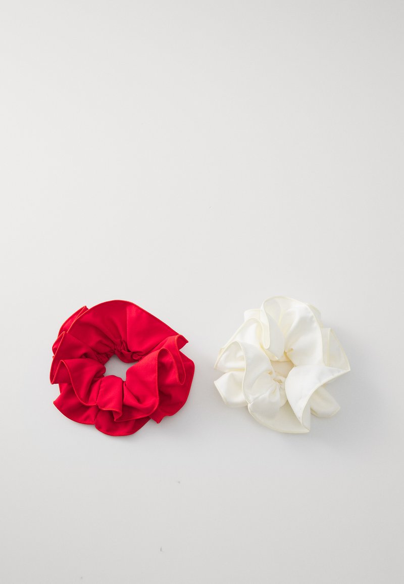 Two scrunchies displayed on a white surface: a red satin one with a ruffled texture on the left and a white satin one with similar ruffles on the right.