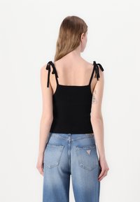 Svart ribbet tanktop med justerbare knyttebånd, tettsittende design; kombinert med lyseblå, løstsittende jeans med baklommer.