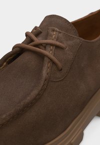 Chaussure à lacets en daim marron avec bout arrondi, coutures détaillées et semelle en caoutchouc marron clair.