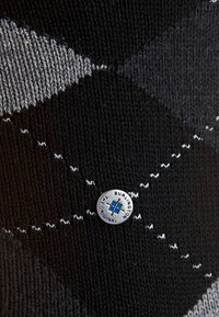 Calzino nero a maglia con motivo a rombi grigio, rifinito con cuciture bianche e un logo circolare argentato con dettagli blu.