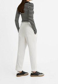 Haut à manches longues rayé noir et blanc, pantalon blanc à coupe décontractée et baskets noires avec accents gris. Accent mis sur des motifs simples et un design casual.