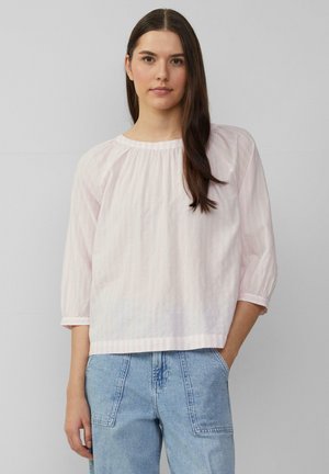 Blouse rayée rose clair avec des manches 3/4, un col rond et un détail froncé. Portée avec un jean en denim bleu clair, doté de poches.