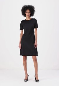 Rochie neagră cu mâneci scurte, cu un corp ajustat și o fustă evazată. Fabricată dintr-un material neted, având un design simplu și detalii discrete de cusătură.