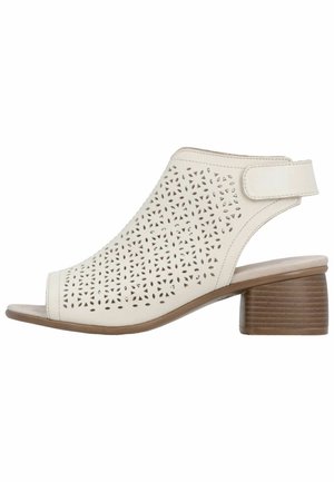 Sandal beige con punta aperta con motivi floreali tagliati al laser, cinturino regolabile in velcro alla caviglia e tacco basso impilato in legno.