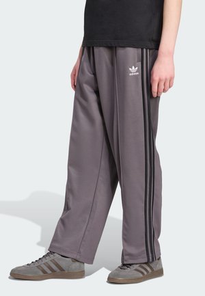 Gray athletic pants with black side stripes, featuring a loose fit and soft texture. Paired with gray shoes displaying three brown stripes.