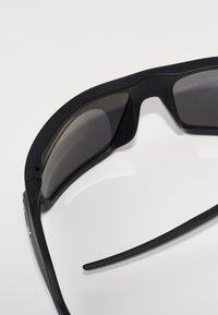 Ochelari de soare negri cu lentile închise, un design elegant și un finisaj mat neted. Au rame curbe și brațe subțiri, alungite.