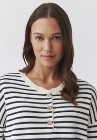 Striped knit top featuring navy and white horizontal stripes, rounded neckline, and three wooden buttons at the front. Smooth texture.